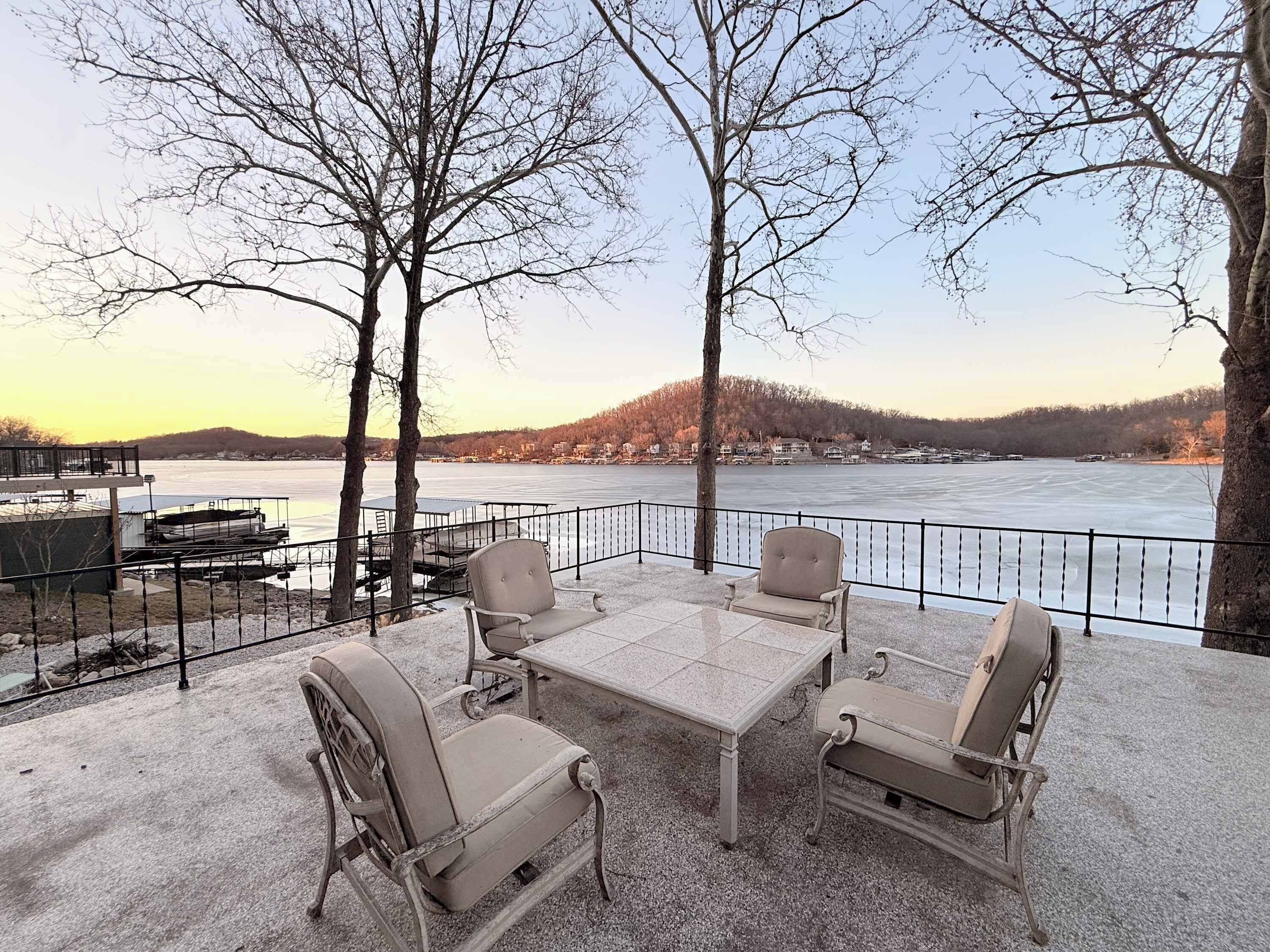 An outdoor seating area with a table and chairs, overlooking a frozen lake with buildings in the background.
