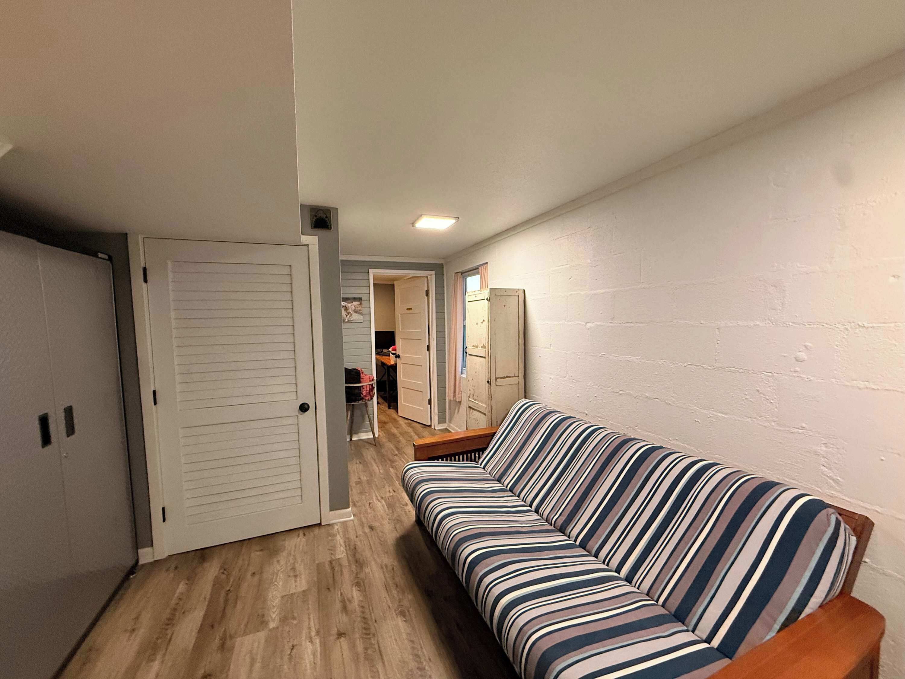 A hallway with a striped sofa, a wooden bench, and a door leading to a room.