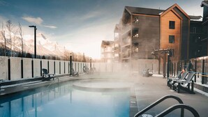 A pool area with lounge chairs, a building with wooden siding, and mountains in the background.