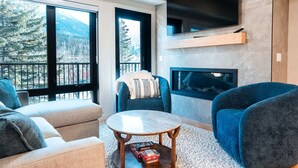 A modern living room with a fireplace, large windows, and a flat-screen TV.