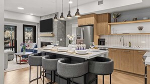 A modern kitchen with a central island, bar stools, and a dining area with a sofa and coffee table.