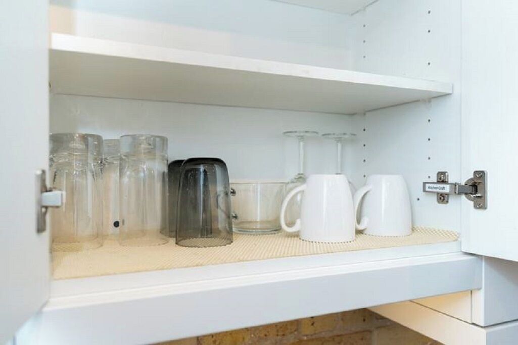 A kitchen cabinet with a coffee maker, several glass mugs, and a tea kettle.