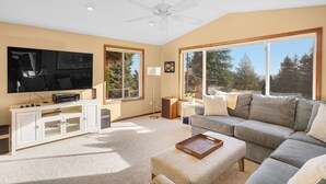 A living room with a large TV, white entertainment unit, grey sofa, and a ceiling fan. - Oregon Wine Country Hillside Retreat w/4 bedrooms, 3 baths. (Dundee)