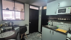 Una cucina compatta con forno a microonde, piano cottura e lavello. È presente un piccolo angolo ristoro con tavolo e sedie.