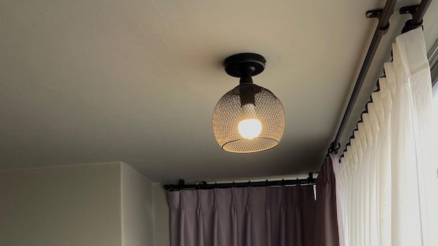 Una stanza con una lampada a soffitto, una tenda e uno scaffale con un televisore.