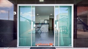 Una entrada de edificio moderno con puerta de vidrio, una cocina a la vista con taburetes de bar y el número '3' en la pared.