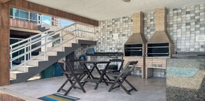 Una cocina moderna con una parrilla integrada, un comedor con mesa y sillas, y una escalera que lleva a un nivel superior.