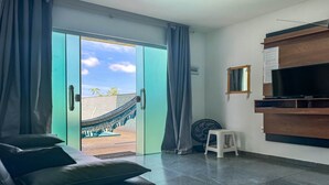 Una habitación moderna con puerta corrediza de vidrio que da a un balcón, un televisor de pantalla plana en la pared, un taburete pequeño y un ventilador de techo.