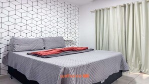 Ett sovrum med en vägg som har ett geometriskt mönster, en säng med grått sänglinne och en grön gardin.