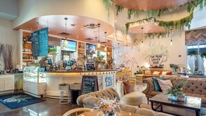 Un café chaleureux avec un bar, des tables et un panneau indiquant : « The Palms Coffee House ».