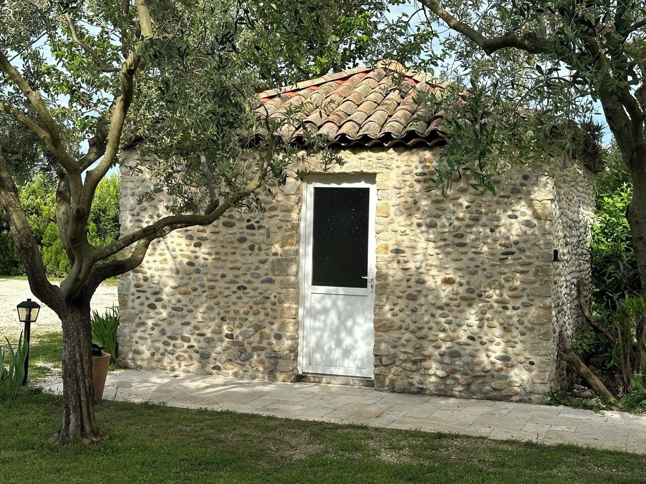 Un edificio de piedra con techo de tejas, puerta blanca y una ventana pequeña.