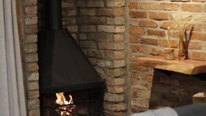 Ein gemütliches Zimmer mit Kamin aus Backsteinen, einem Holzstuhl und einem Tisch mit einer Vase.