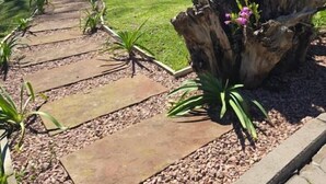 Ein Gartenpfad mit einer hölzernen Pergola und einem großen Baumstumpf mit rosafarbenen Blüten.