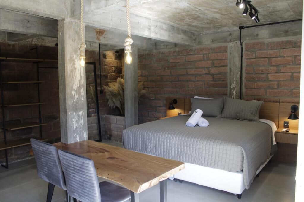 Un dormitorio con cama, mesita de noche, lámpara y un escritorio de madera con silla.