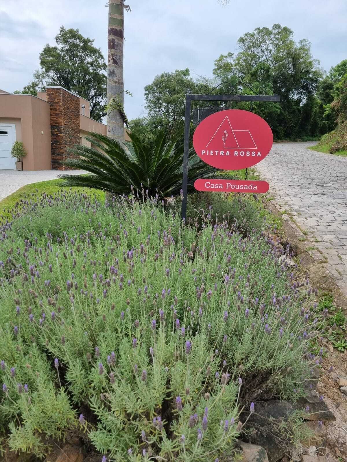 Un cartel que dice 'PIETRA ROSSA Casa Pousada', con un muro de piedra y plantas de lavanda al frente.