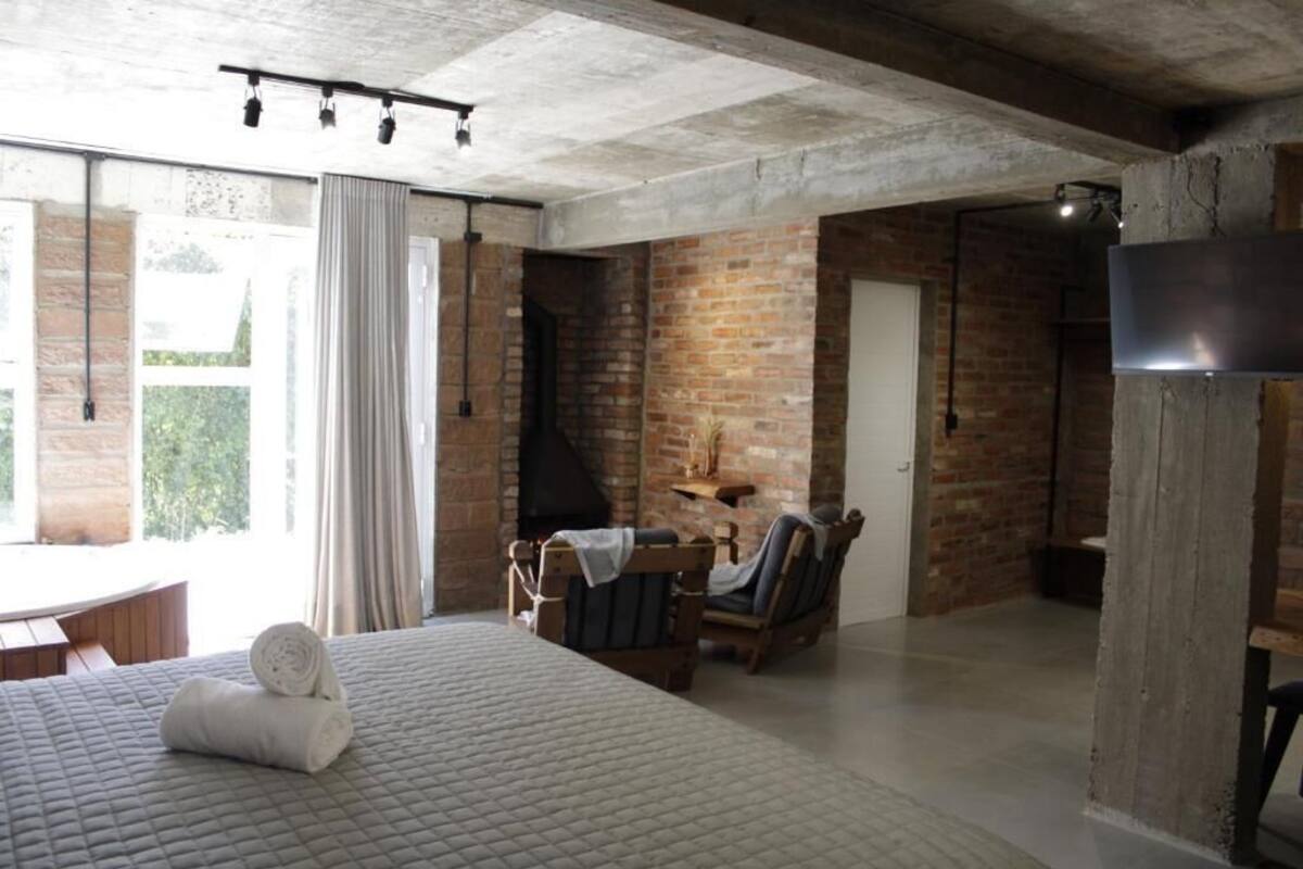 Una habitació amb un llit, una taula, cadires, una llar de foc i una finestra gran.