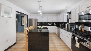 Una cucina moderna con mobili bianchi, un piano di lavoro nero, elettrodomestici in acciaio inossidabile e luci a sospensione.