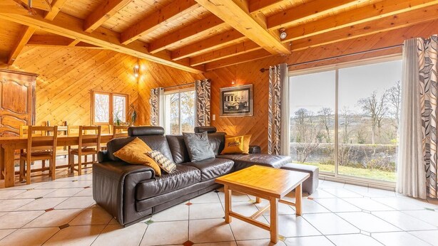 Ein gemütliches Wohnzimmer mit Holzboden, einer schwarzen Ledersofa, einem Holztisch und einem großen Fenster mit Blick ins Freie.