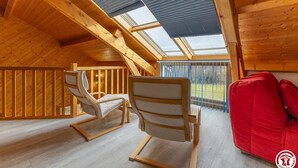 Ein Holzinnenraum mit schrägverdachter Decke, zwei Schaukelstühlen und einem roten Sofa.