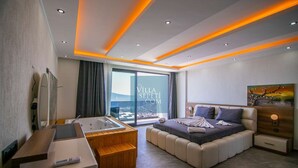 A modern hotel room with a large bed, a separate bathroom with a bathtub, a desk, and a view of the city. - Villa in Kalkan with infinity pool, sauna and Turkish bath. (Antalya)