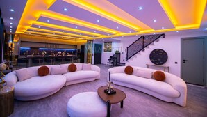 A modern living room with two white sofas, a round ottoman, and a staircase with a geometric railing. - Villa in Kalkan with infinity pool, sauna and Turkish bath. (Antalya)
