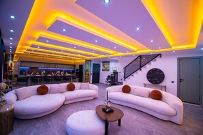 Uma sala de estar moderna com dois sofás brancos, um banquinho redondo e uma escada com guarda-corpo geométrico.