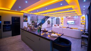 A modern kitchen with a central island, built-in appliances, and a dining area with a sofa and TV. - Villa in Kalkan with infinity pool, sauna and Turkish bath. (Antalya)