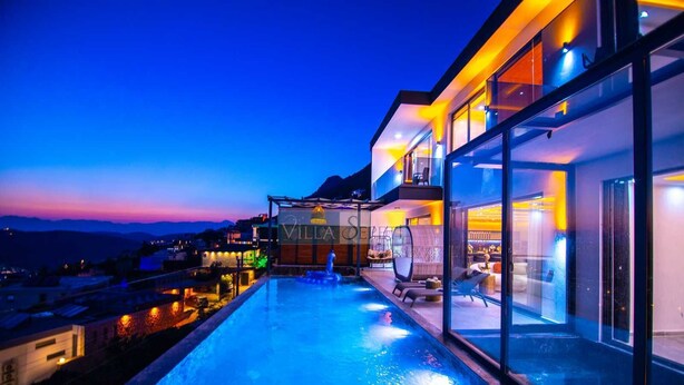 A modern villa with a rooftop infinity pool, glass walls, and a view of the surrounding landscape. - Villa in Kalkan with infinity pool, sauna and Turkish bath. (Antalya)