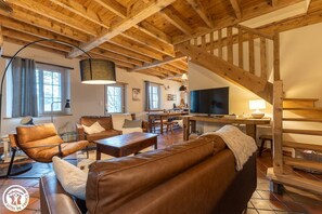 Ein geräumiges Wohnzimmer mit hohen Holzbalken, Ledersofas, einem Essbereich und einer Treppe.