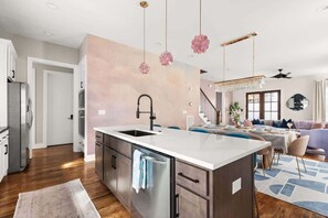 A modern kitchen with a central island, stainless steel appliances, and a hanging floral chandelier. - New Luxury Home near Nissan Stadium |  Sleeps 12 (Nashville)