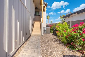 A narrow pathway leading to a staircase, surrounded by white walls and a gravel area with pink flowers. - Executive Duplex Rental in Walkable Downtown Chandler (Chandler)