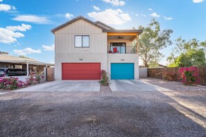 A two-story house with a red and blue garage, a balcony with a red chair, and a wooden fence with pink flowers. - Executive Duplex Rental in Walkable Downtown Chandler (Chandler)