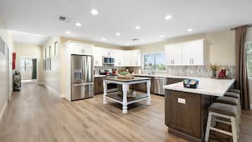 Cocina moderna con armarios blancos, electrodomésticos de acero inoxidable, una isla central y vistas al exterior.