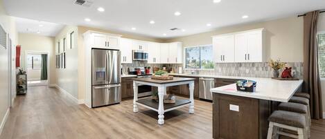 A modern kitchen with white cabinetry, stainless steel appliances, a central island, and a view to the outside.
