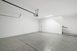 Een ruime, lege kamer met een schuine kap, een aan het plafond bevestigde projector en een deur aan de rechtermuur.