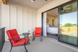 Ein Balkon mit zwei roten Stühlen, einem kleinen Tisch und einer Glasbalkontür, die zu einem Schlafzimmer mit einem Bett und einem Nachttisch führt.