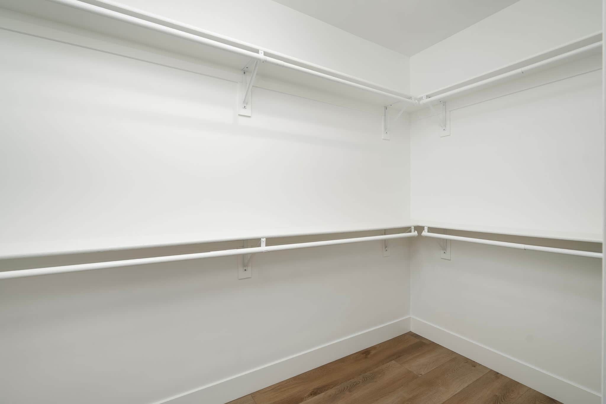 Esquina de una habitación con paredes blancas y suelo de madera, con estanterías blancas fijadas al techo.