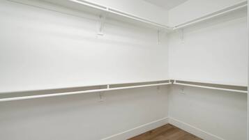 Esquina de una habitación con paredes blancas y suelo de madera, con estanterías blancas fijadas al techo.