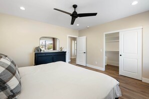 Une chambre à coucher comprenant un lit, une commode, un ventilateur de plafond et un dressing.