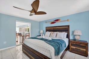 A bedroom with a bed, wooden headboard, two nightstands, a ceiling fan, and a view through a glass door to an outdoor area. - Spacious Beach House with Ocean Access, Beach and Restaurants (Port Charlotte)