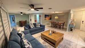 Sala de estar com sofá azul, mesa de centro de madeira e ventiladores de teto.