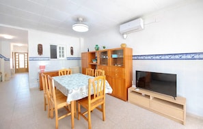 Un coin repas avec une table et des chaises, un meuble avec des portes en verre, un téléviseur posé sur un meuble et un ventilateur de plafond.