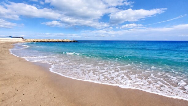 A beach with clear blue water, a sandy shore, and a rocky breakwater in the background. - Lovely home in Sueca with WiFi (Sueca)