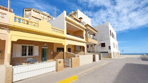 A coastal street with multi-story buildings, including a yellow building with a balcony and a white building with a garage. - Lovely home in Sueca with WiFi (Sueca)