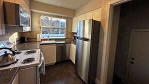 A compact kitchen with white cabinets, stainless steel appliances, and a window providing natural light.
