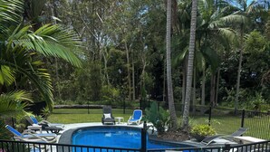 Ein Swimmingpool, umgeben von einem schwarzen Metallzaun, mit Liegestühlen und einer Feuerstelle im Vordergrund.