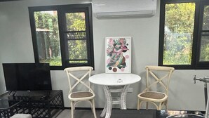 Ein Zimmer mit zwei Korbstühlen, einem kleinen weißen Tisch, einem Fernseher und einem Gemälde an der Wand.
