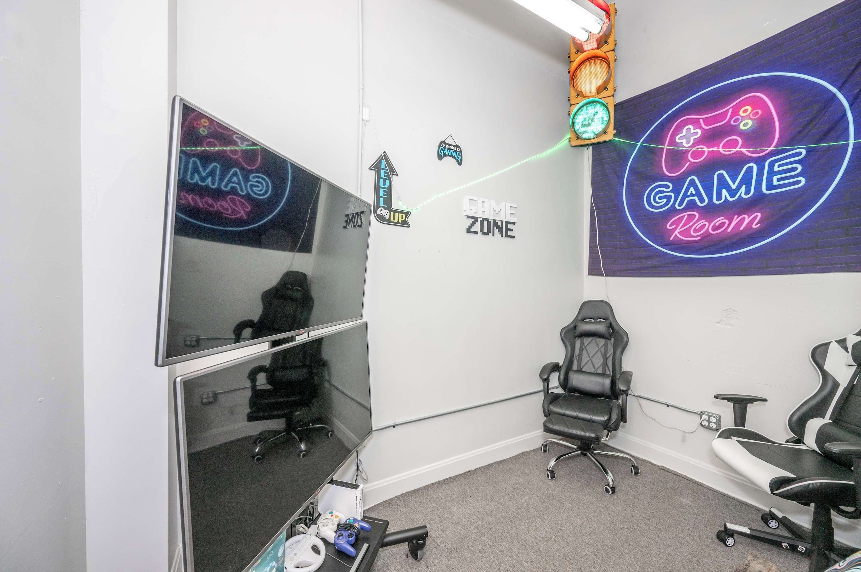 A gaming room with a neon sign, gaming chairs, and a desk with a computer.