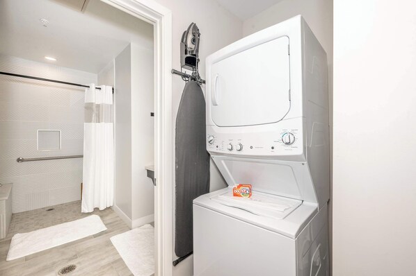 A laundry area with a front-loading washer and dryer, a towel rack, and a shower with a glass door. - The 333 Suites 2nd Floor Retreat (Cincinnati)