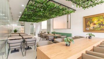 A modern conference room with a long wooden table, several chairs, and a green plant hanging from the ceiling.